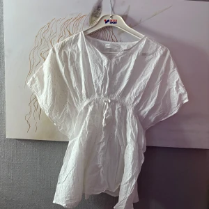 Vit blus med glittriga detaljer från Zara - Superfin vit blus från Zara med glittriga trådar och små paljetter. Blusen har v-ringning, korta vida ärmar och resår i midjan som ger en snygg siluett. Perfekt för dig som gillar en luftig och lätt stil med lite extra bling.