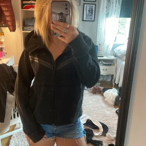 Svart hoodiejacka från Nike - Svart hoodiejacka från Nike med dragkedja framtill och huva. Jackan har diskreta svarta detaljer över bröstet och är tillverkad i mjukt bomullsmaterial. Perfekt för en sportig och avslappnad stil.