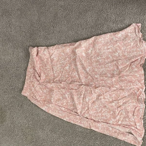 Ljusrosa blommig långkjol - Säljer en superfin ljusrosa långkjol med vitt blommigt mönster. Kjolen har en mjuk och flowy känsla, perfekt för dig som gillar romantisk och feminin stil. Passar dig som vill ha en chill och snygg look till våren eller sommaren.