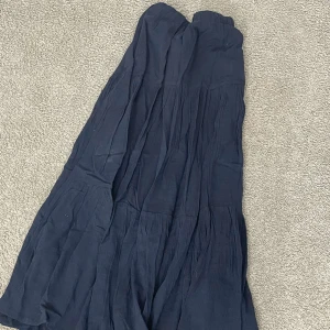 Mörkblå långkjol i bomull - Säljer en mörkblå långkjol med volangdetaljer. Kjolen har en luftig och skön känsla, perfekt för dig som gillar avslappnad stil. Materialet är mjukt och lätt bomull, vilket gör den bekväm att bära under varmare dagar.