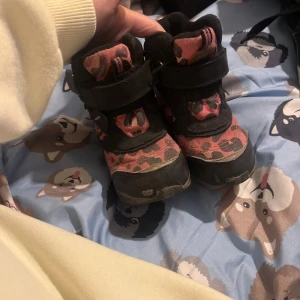 Nordbjørn rosa leopardmönstrade kängor (barn) - Tuffa kängor från Nordbjørn i svart och rosa med leopardmönster. Skorna har praktiska kardborreband och robust sula, perfekta för lek utomhus. Materialmix av syntet och skinn ger både stil och funktion.