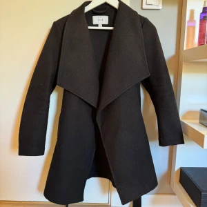 Svart kappa från Vila - Jättesnygg svart kappa från Vila med knytbälte i midjan!! Mycket gott skick!!