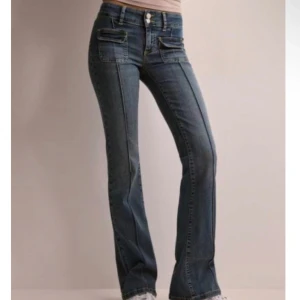 Blå bootcut jeans med fickdetaljer från Nelly - Snygga blå jeans med bootcut passform och markerade sömmar längs benen. Byxorna har dubbla framfickor med lock och dragkedja, samt hög midja och klassisk jeanslook. Perfekta för en trendig och avslappnad stil. Som nya!