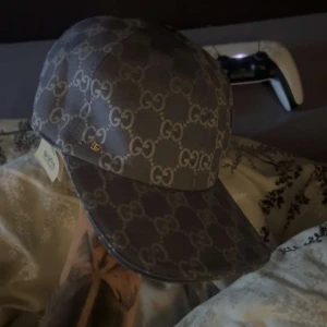 Gucci keps med GG-mönster - Snygg keps från Gucci i mörkgrått med det klassiska GG-monogrammet över hela kepsen. Justerbar rem baktill och insida i ljus textil. Perfekt accessoar för dig som vill sticka ut med lyxig streetstyle.