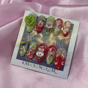 Minsung MelonPop (XS);Medium Almond - Set med 10 handgjorda press-on naglar i dn medium mandelform. Designen har mix av rött, grönt och vitt med 3D-dekorationer som hjärta, regnbåge, kanin, katt och rosetter. Glittriga detaljer, pärlor och stenar ger extra wow-effekt. Perfekt för dig som älskar unik och färgglad nagelkonst. I storlek XS: 14 mm, 11 mm, 11,5 mm, 10 mm, 8 mm 