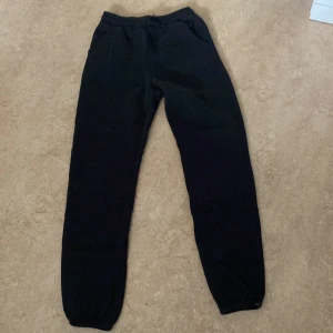 Svarta mjukisbyxor med NYC-brodyr - Svarta mjukisbyxor med broderad NYC-logga vid fickan. Byxorna har resår i midjan och vid bensluten för en skön och avslappnad passform. Perfekta för chill dagar eller när du vill vara bekväm men ändå se snygg ut.