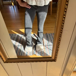 Grå bootcut jeans med slitning - Säljer ett par grå jeans med bootcut-modell och snygg slitning vid låret. Jeansen har klassisk femficksdesign, låg midja och är i mjukt denimtyg. Perfekta för dig som gillar en avslappnad men trendig look.