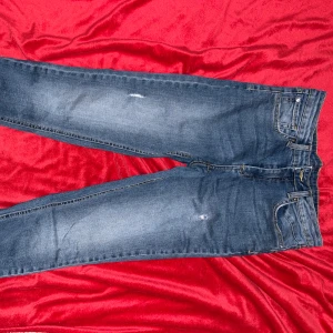 Blå korta jeans - Säljer ett par klassiska blå korta jeans med lätt slitna detaljer på benen. Jeansen har fem fickor, normal passform och raka ben. Perfekta för en avslappnad och stilren look. Materialet är mjukt och bekvämt denim.