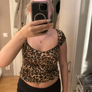Leopardmönstrad croppad topp - Säljer en croppad topp med leopardmönster och korta ärmar. Toppen har en snygg, rundad urringning och sitter tight mot kroppen. Perfekt för dig som vill sticka ut med ett djurmönster och gillar trendiga plagg.