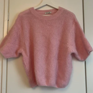 Rosa stickad tröja från Design by si  - Supermysig oanvänd rosa stickad tröja från  design by si med korta ärmar och rund hals. Tröjan har en fluffig och mjuk känsla, perfekt för dig som gillar en chill och söt stil. 
