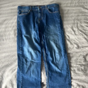 Blå Lee jeans straight fit - Säljer ett par klassiska blå jeans från Lee med raka ben och normal passform. Jeansen har fem fickor, tydliga kontrastsömmar och Lee-logga på bakfickan. Perfekta för dig som gillar en tidlös denimlook.