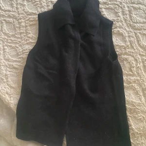 Svart stickad väst med krage - Svart stickad väst från H&M med bred krage och ribbade kanter. Perfekt att slänga över en skjorta eller t-shirt för en chill och stilren look. Enkel design med två knappar, vilket gör den lätt att matcha med allt.