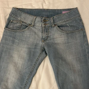 Ljusblå jeansbyxor från Up Jeans - Säljer ett par klassiska ljusblå jeansbyxor från Up Jeans med raka ben och dubbla knappar i midjan. Jeansen har fem fickor och snygga slitningar för en avslappnad look. Perfekta till vardags och lätta att matcha med olika stilar.