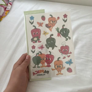 Klistermärken/tatueringar - En färgglad bok med tecknade paprikor och andra grönsaker i roliga poser, perfekt för unga som gillar mat, pyssel och kreativitet. Boken verkar vara lekfull och inspirerande, med klistermärken och illustrationer som gör den extra rolig.