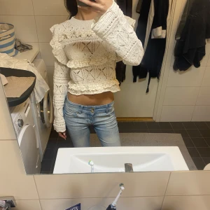 Vit stickad croppad blus med volanger - Superfin vit stickad blus med volangdetaljer och genombrutet mönster. Croppad modell med långa ärmar och rund halsringning. Perfekt för dig som gillar romantisk och trendig stil. Snygg till både jeans och kjol!