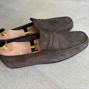 Bruna mocka loafers Tod’s - Säljer ett par stilrena bruna Tod’s loafers i brun mocka med klassisk design. Skorna har diskreta sömmar och platt sula,y perfekta för en dressad look. Storlek 41 herr.