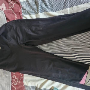 Svarta leggings med rosa detalj - Svarta leggings med en liten rosa/grå detalj vid benslutet. Sitter tight och är gjorda i ett stretchigt syntetmaterial som passar perfekt till träning eller chill. Enkla att matcha med det mesta och superbekväma.