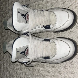 Nike Air Jordan 4 midnight navy - Nike Air Jordan 4 midnight navy med vit ovandel i skinn, grå och svarta detaljer samt specklad grå sula. Klassisk Jumpman-logga på plösen och hälen. Skorna har meshpaneler och snörning för en ikonisk look. Perfekta för dig som vill sticka ut med en retro vibe.