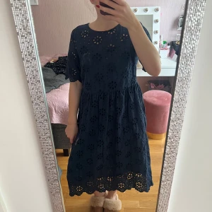 Mörkblå broderad klänning med öppen rygg - Supersöt mörkblå klänning i bomull med broderade blommor och hålmönster. Klänningen har korta ärmar, rund hals och en snygg öppen rygg med knapp. Den är vadlång och har en luftig, flowy passform som känns både chill och stilren. Jag har storlek S i vanliga fall och så här sitter den på mig. 