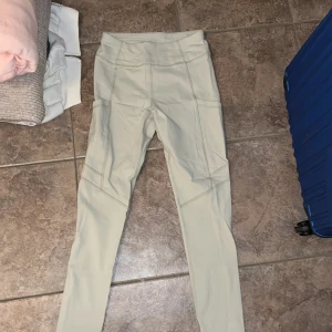 Beige leggings från SOC med fickor - Snygga beige leggings från SOC med hög midja och praktiska sidofickor. Tillverkade i stretchigt syntetmaterial som andas, perfekta för träning eller chill. Snygga sömdetaljer längs benen för extra stilpoäng.