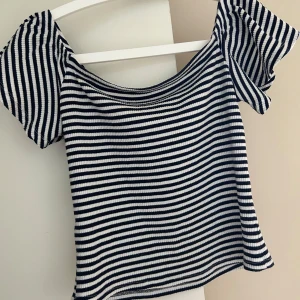 Randig ribbad topp med kort ärm - Säljer en marinvit  ribbad topp med smala horisontella ränder och korta ärmar. Toppen har en rundad halsringning och är tillverkad i bomull material. Perfekt för en avslappnad stil.