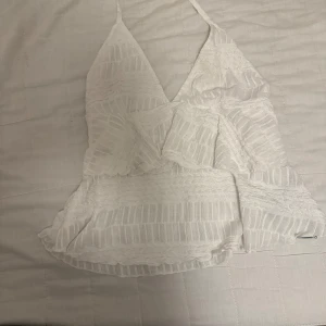 Vit volangig linnetopp med spetsdetaljer - Säljer en söt vit linnetopp med volanger och tunna axelband som du knyter runt halsen. Toppen har spetsdetaljer och ett lätt transparent tyg med struktur. Perfekt för varma dagar och somriga outfits. Köpt på Nelly 