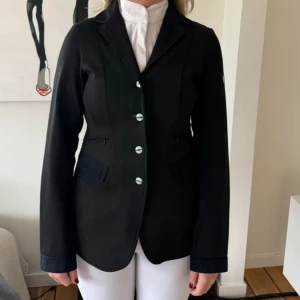 Svart ridkavaj från Equiline - Säljer denna svarta kavaj från Animo. Storlek 12 år och passar större storlekar också. Tjejen på bilden är 18 år och 160 lång. Mycket bra skick, sparsamt använd.