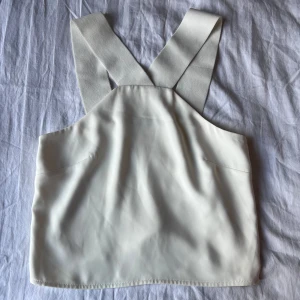 Vit croppad linnetopp från Bik Bok - Säljer en stilren vit linnetopp från Bik Bok i storlek XS. Toppen är croppad med breda axelband som korsas i ryggen och har en enkel, clean design. Perfekt att matcha med höga jeans eller kjol för en fräsch look.