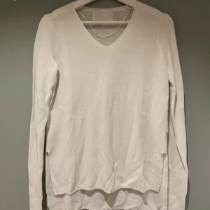 Vit v-ringad långärmad tröja - En stilren vit långärmad tröja med v-ringning. Tröjan är tunn och har en klassisk passform, perfekt att matcha med jeans eller kjol. Materialet känns mjukt och lätt, vilket gör den skön att bära under flera säsonger. Slits i sidan och faller lite längre baktill. 