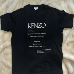 Svart Kenzo t-shirt med tryck - Svart t-shirt från Kenzo med vit text och tryck framtill. Klassisk rund halsringning och korta ärmar. T-shirten är i bomull och har en clean, stilren look med statement-tryck som ger en cool vibe.