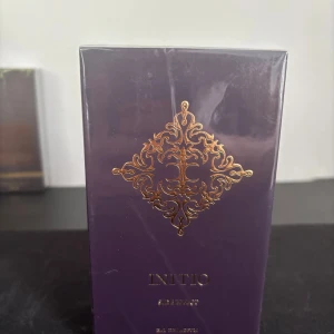 Initio parfym side effect  - Exklusiv parfym från Initio i en elegant mörklila kartong med guldfärgat dekorativt mönster på framsidan. Förpackningen är rektangulär och plastad, vilket ger en lyxig känsla. Perfekt för dig som gillar unika och sofistikerade dofter.