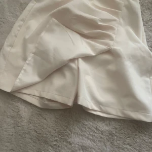Vit omlottkjol från Chiquelle - Säljer en stilren cream färgade shortskjol från Chiquelle i storlek large. Shortskjolen har en kort längd och är tillverkad i ett mjukt, slätt material. Perfekt att matcha med en enkel topp för en fräsch look.