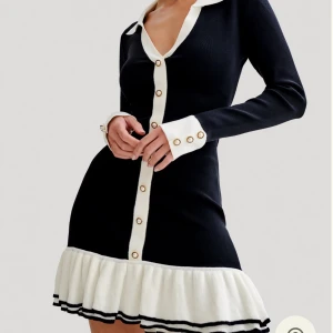 Svart/vit klänning med knappar Meshki Pareesa - Säljer en svart klänning med vita detaljer, lång ärm och djup v-ringning. Klänningen har dekorativa knappar framtill och en volangkant nertill i vitt med svarta ränder. Modellen är figurnära med markerad midja. Använts bara en gång därför nästan nyskick!🌸