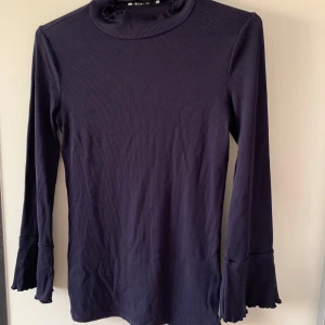 Mörkblå ribbad polotröja med volangärm - Snygg mörkblå ribbad polotröja från Ginatricot med volangdetalj vid ärmsluten. Liten i storlek, mer som xs-s.