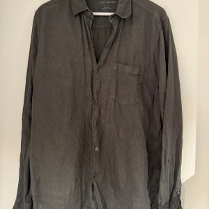 Mörkgrön linneskjorta från A Day's March - Snygg mörkgrön skjorta i linne från A Day's March. Klassisk krage, bröstficka och knäppning framtill. Långärmad modell med avslappnad passform, perfekt till jeans eller chinos. Enkel och stilren design som funkar året runt.