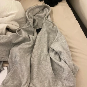 Grå hoodie med dragkedja - Mysig grå hoodie med dragkedja och huva. Tröjan har en relaxed passform, stora fickor framtill och justerbar snörning i huvan. Perfekt för chill dagar eller när du vill vara extra bekväm. Tillverkad i mjuk bomullsblandning.