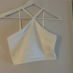 Vit croppad linnetopp från Divided - Säljer en vit croppad linnetopp från H&M med tunna axelband. Toppen har en enkel och clean look, perfekt till jeans eller kjol. Mjuk och stretchig bomullskänsla för en bekväm passform.