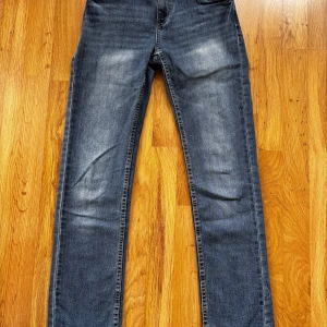 Levi's 511 blå jeans straight fit - Säljer ett par klassiska Levi's 511 jeans i blå denim med snyggt slitna detaljer. Jeansen har raka ben, fem fickor och Levi's ikoniska läderpatch bak. Perfekt passform och tidlös look som funkar till allt.
