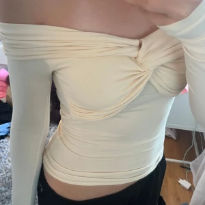 Offshoulder cremevit topp - Säljer en cremevit offshoulder topp med lång ärm och snygg twist-detalj framtill. Toppens material är stretchigt och sitter tight mot kroppen. Slutsåld från Gina tricot. Storlek XS men funkar även på mig som brukar ha S💛🤍