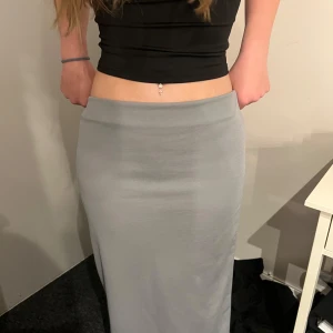 Ljusgrå långkjol - Säljer en stilren ljusgrå långkjol med rak passform. Kjolen är enkel och minimalistisk, perfekt att matcha med olika toppar. Materialet känns mjukt och följsamt mot kroppen.