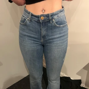 Blå högmidjade skinny jeans från Gina Tricot - Säljer ett par klassiska blå skinny jeans från Gina Tricot med hög midja och fem fickor. Jeansen har en smal passform och stängs med dragkedja och knapp. Perfekta till vardags och enkla att matcha med olika toppar.