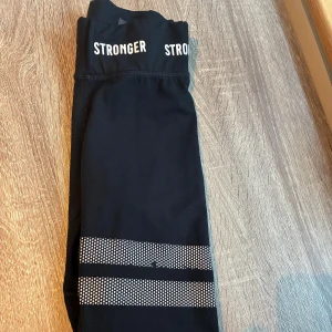 Svarta tights från Stronger xs - Svarta tights från Stronger med hög midja och logga runt linningen. Snygga vita prickiga ränder på ena benet ger en sportig vibe. Stretchigt material som passar perfekt till träning eller chill. Tight passform och bekväma att bära hela dagen. 