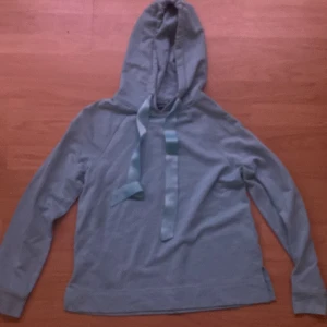 Ljusblå hoodie från KappAhl - Säljer en ljusblå hoodie från KappAhl med långa ärmar och huva. Tröjan har breda dragsnören vid halsen och är tillverkad i mjukt material, perfekt för en avslappnad stil.