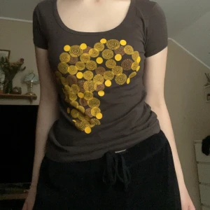 Brun t-shirt med Afrika-tryck från Electric Zulu - Säljer en brun t-shirt från Electric Zulu i storlek M. T-shirten har ett unikt tryck av Afrikas kontinent i gult och mönstrat på bröstet. Modellen är klassisk med rund hals och korta ärmar. Perfekt för dig som gillar statement-plagg! Små fläckar längst ner på tröjan, se bild 5.