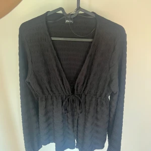 Svart långärmad kofta med knyt - Aldrig använd!! Svart långärmad kofta från Gina Tricot med struktur i tyget och knyt framtill i midjan. Djup v-ringning och lätt croppad passform. Perfekt att slänga över en topp för en chill look. Storlek S🤍