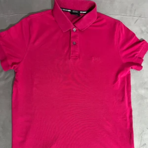 Hugo Boss pikétröja   - Snygg  pikétröja från Hugo Boss i mjuk pima-bomull. knäppning med två knappar och diskret broderad logga på bröstet. Perfekt för dig som vill ha en stilren och fräsch look med premiumkänsla.