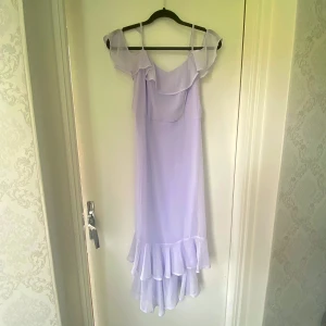 Ljuslila volangklänning med axelband - Superfin ljuslila långklänning med tunna axelband och volangdetaljer både upptill och nertill. Klänningen har offshoulder-ärmar och är gjord i ett lätt, flowy material som känns perfekt för sommarens alla tillfällen.