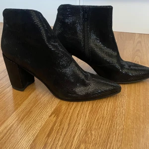 Svarta boots från Vagabond - Snygga svarta boots från Vagabond med en glittrig yta och spetsig tå. De har en bekväm klack och dragkedja på sidan för enkel på- och avtagning. Perfekta för att ge en elegant touch till din outfit.