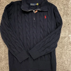 Svart stickad tröja från Polo Ralph Lauren - Säljer en stilren svart stickad tröja från Polo Ralph Lauren med dragkedja och röd broderad logga på bröstet. Tröjan har långa ärmar och ribbade detaljer vid krage och ärmslut. Perfekt för kyliga dagar! Skick 9/10. Enda defekt är att industrilappen är avklippt. Annars verkar allt vara bra. Nypris är cirka 2200. Storlek medium men har krymt så är lite mer åt small hållet än large. Hör av dig om du undrar något👍