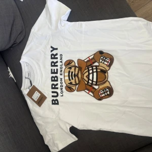 Vit t-shirt från Burberry - Säljer en vit t-shirt från Burberry med ett stort tryck av en nalle på framsidan. Helt oanvänd med lappar! Priset är inte skrivet i sten.